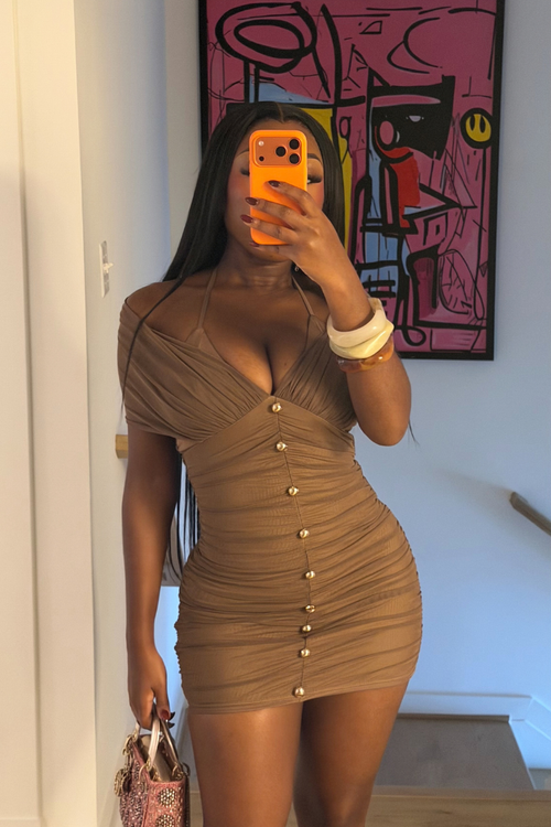 Woman wearing Demuluxe Amira Dress, a mocha off shoulder ruched mini dress with gold button trim