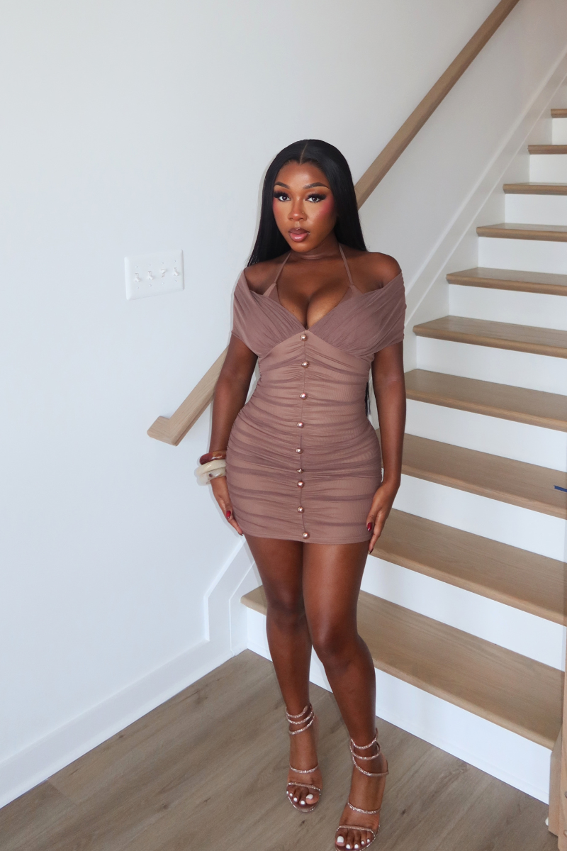 Woman wearing Demuluxe Amira Dress, a mocha off shoulder ruched mini dress with gold button trim