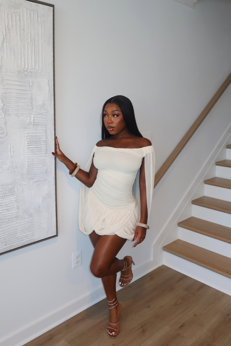 Woman wearing Demuluxe Brielle Mini Dress, a white draped mini dress with cape sleeves