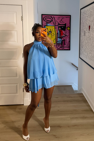 Woman wearing Demuluxe Wisp Halter Dress, a light blue chiffon mini with high halter neck and tiered ruffle skirt
