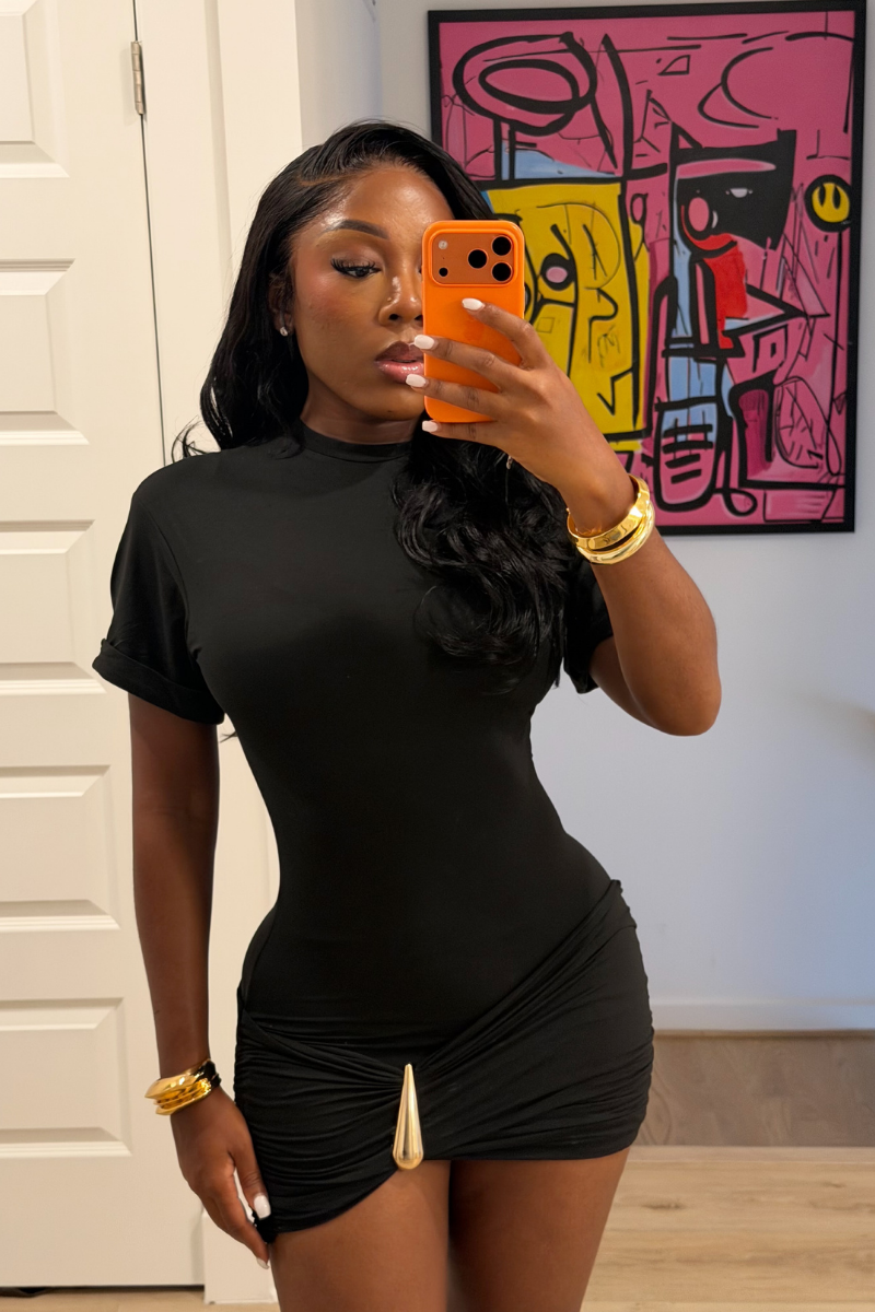 Woman wearing Demuluxe Nyla Mini Dress, a black mock-neck mini dress with ruched hip detail and gold hardware