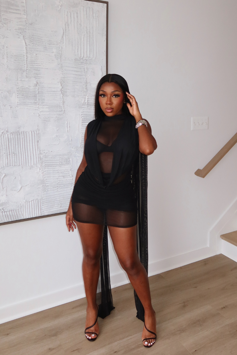 Woman wearing Demuluxe Yara Mini Dress, a sheer mesh mini dress with draped cowl front and long flowing train