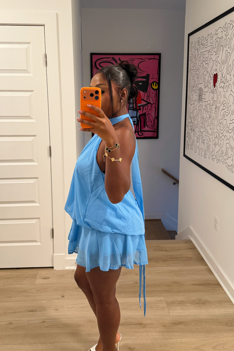 Woman wearing Demuluxe Wisp Halter Dress, a light blue chiffon mini with high halter neck and tiered ruffle skirt