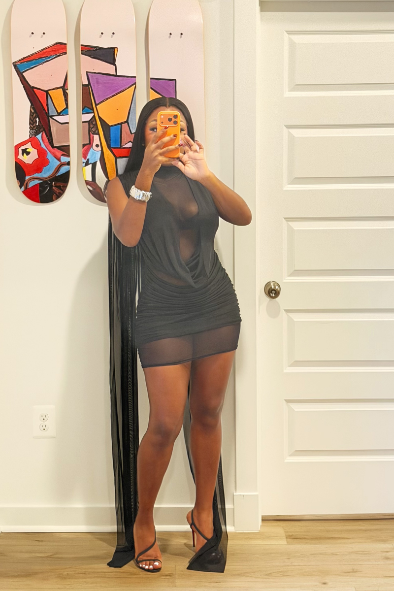 Woman wearing Demuluxe Yara Mini Dress, a sheer mesh mini dress with draped cowl front and long flowing train